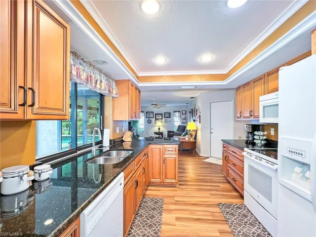 Kitchen featuring light wood-type flooring, white appliances, a tray ceiling, ceiling fan, and sink