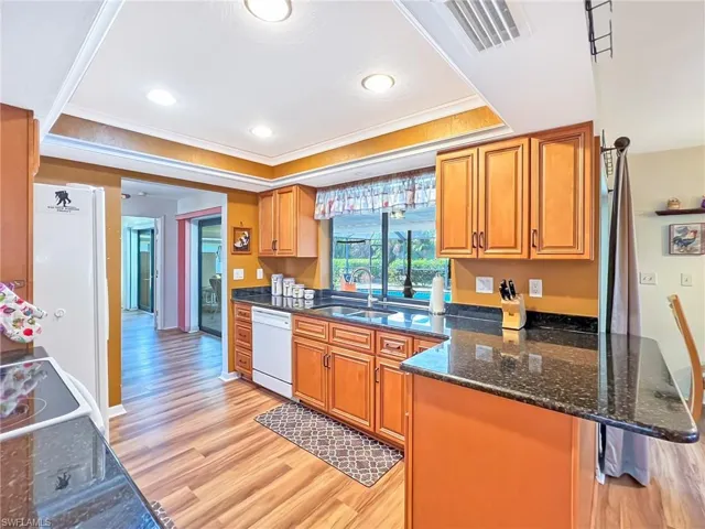 Kitchen featuring light hardwood / wood-style flooring, white appliances, sink, and a tray ceiling