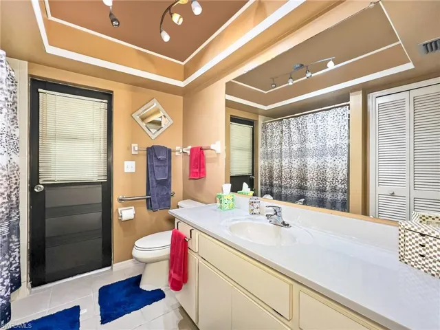 Bathroom featuring tile patterned flooring, vanity, a raised ceiling, and toilet