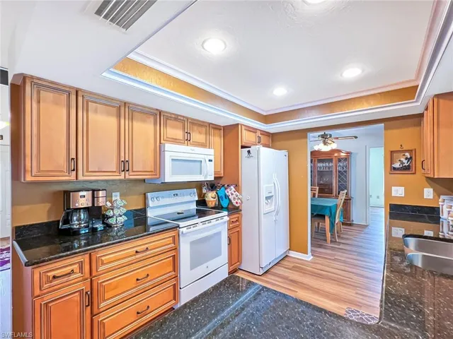 Kitchen with light wood-type flooring, white appliances, a raised ceiling, and sink