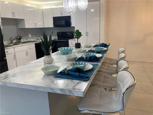 Kitchen with light tile flooring, black appliances, sink, white cabinets, and a chandelier