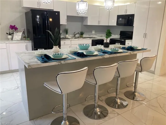 Kitchen featuring black appliances, white cabinets, a kitchen island, and light tile floors