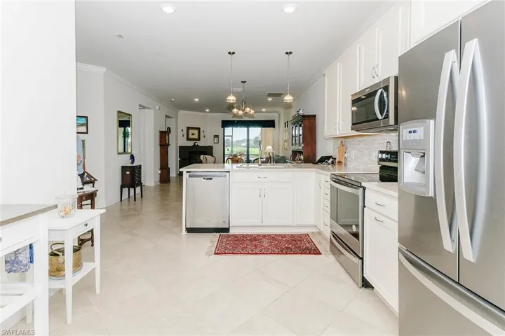 Kitchen with appliances with stainless steel finishes, white cabinets, a peninsula, hanging light fixtures, and quartz countertops.