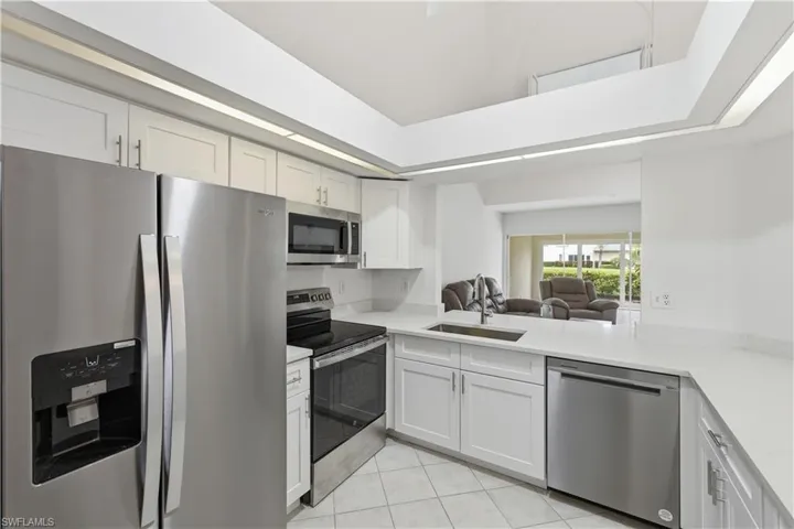 Modern kitchen featuring stainless steel appliances, white cabinetry, a double-basin sink with a gooseneck faucet, light-toned countertops, and tiled flooring