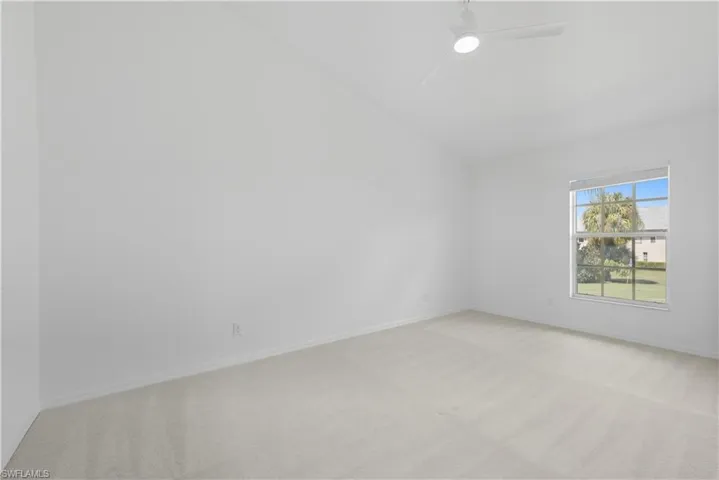 Spare room with light carpet, vaulted ceiling, and a ceiling fan