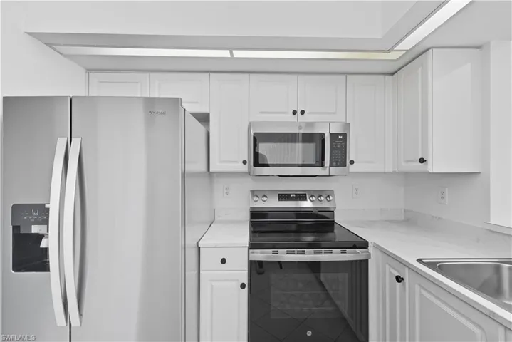 Kitchen featuring stainless steel appliances, white cabinets, and light stone counters