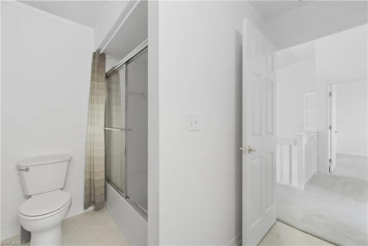 Bathroom with shower / bath combination with glass door, light tile patterned flooring, ornamental molding, and light colored carpet