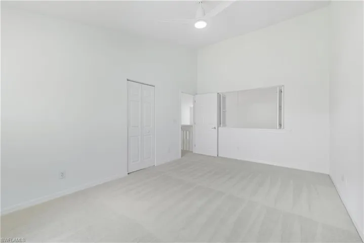 Unfurnished bedroom featuring light carpet, a closet, ceiling fan, and a towering ceiling