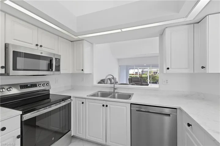 Kitchen with appliances with stainless steel finishes, white cabinets, light stone countertops, and light tile patterned floors