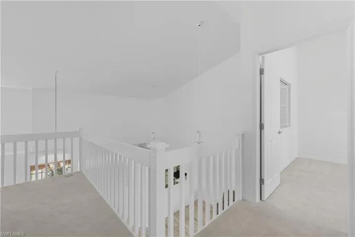 Hallway with light carpet, vaulted ceiling, and an upstairs landing