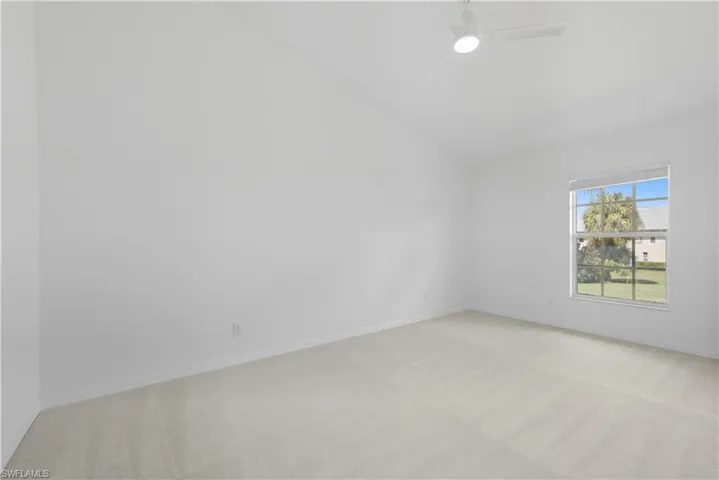 Spacious room featuring vaulted ceilings, neutral-toned carpeting, a window providing natural light, and a ceiling fan with integrated lighting