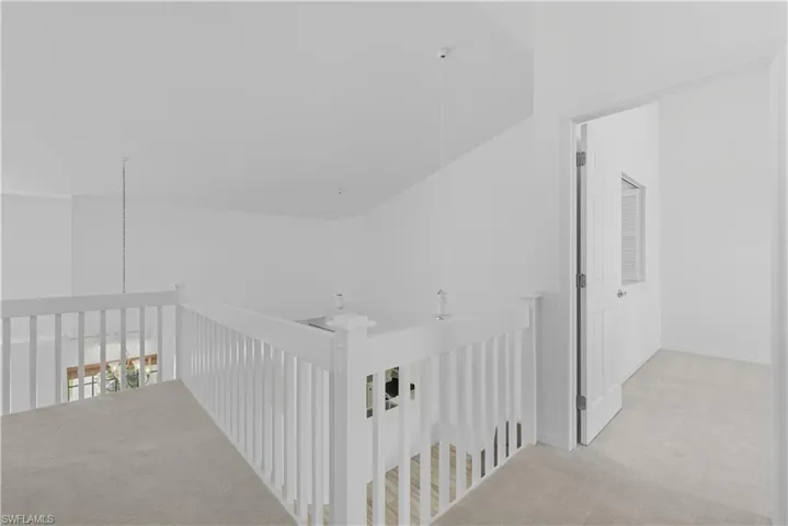 Upper level landing with white balustrade overlooking lower level, featuring neutral carpet flooring, recessed lighting, and a white paneled door with window insert