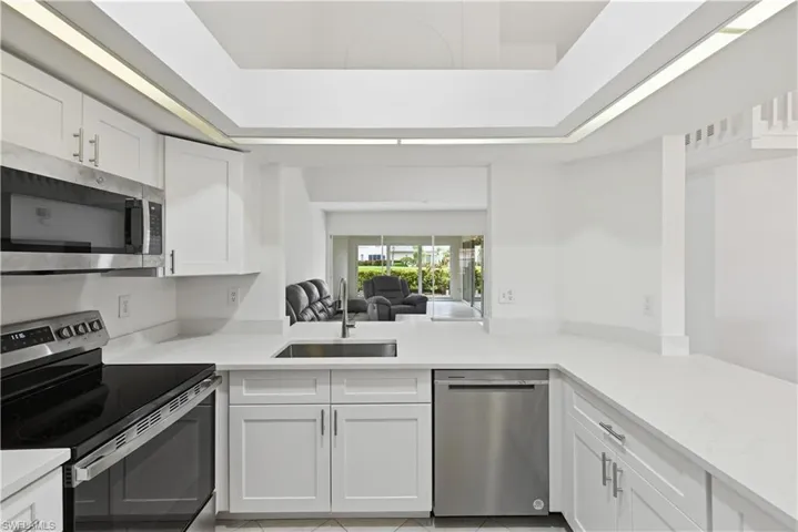 Kitchen featuring white cabinetry, light-toned countertops, a stainless steel sink with a gooseneck faucet, a stainless steel microwave, and a stainless steel dishwasher