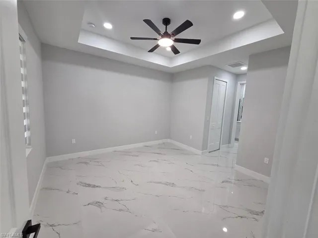 Spacious room with large-format marble-look tile flooring, gray walls, and a tray ceiling with recessed lighting