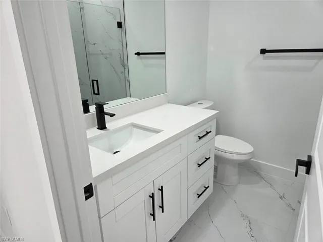 Modern bathroom featuring a white vanity with integrated sink, matte black fixtures, a white toilet, and large format marble-look floor tiles