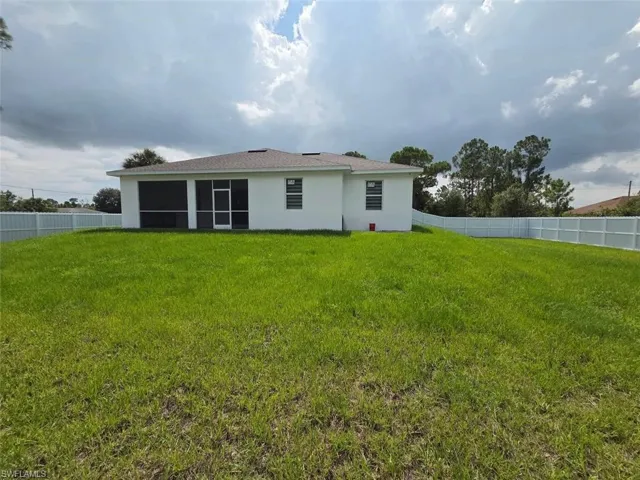 Expansive grassy backyard with a white privacy fence