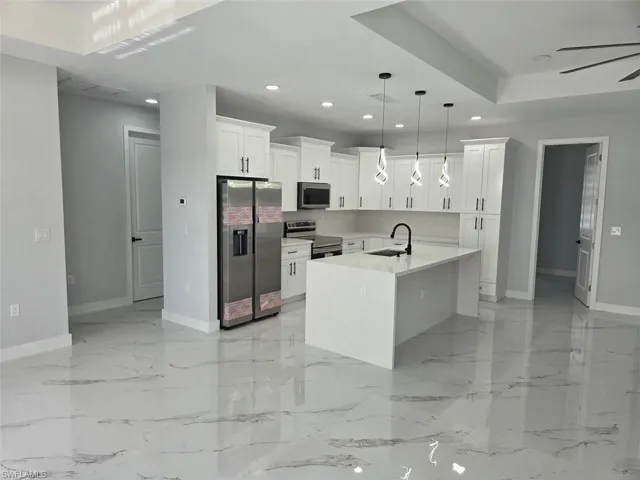 Modern kitchen featuring white shaker cabinetry, stainless steel appliances, a center island with an undermount sink, and contemporary pendant lighting