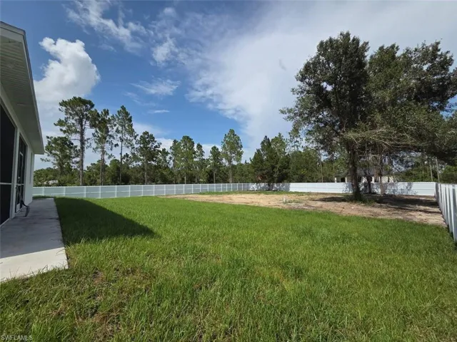Expansive backyard featuring a manicured lawn, a large mature tree, and a full perimeter white privacy fence