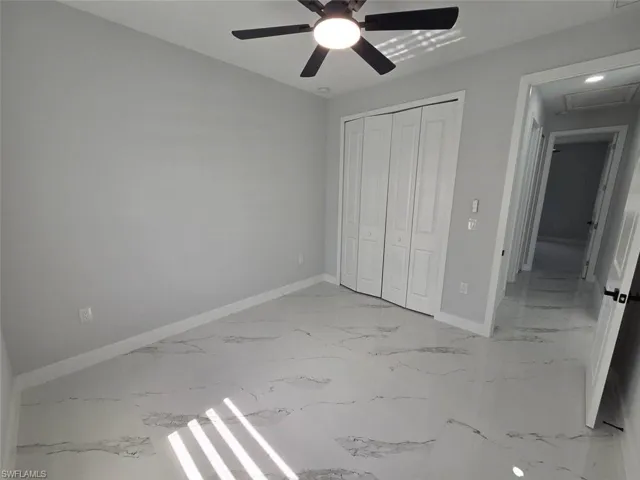 Bright interior space featuring large format white tile flooring with grey veining, neutral wall tones, and a ceiling fan with integrated lighting