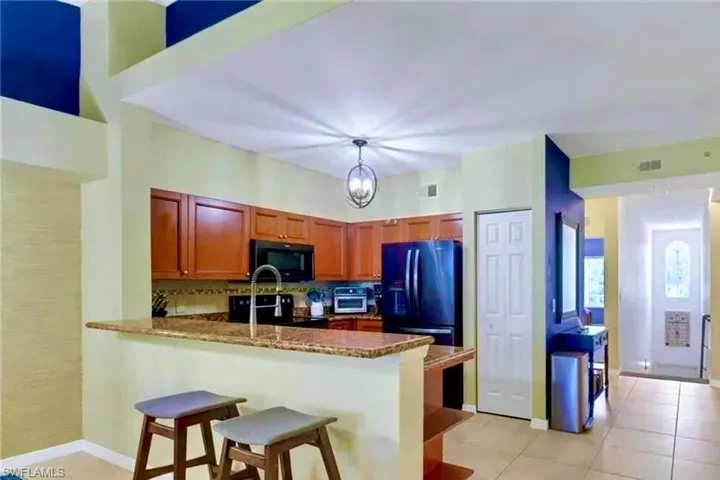 Kitchen featuring a peninsula, black appliances, dark stone countertops, hanging light fixtures, and light tile patterned flooring