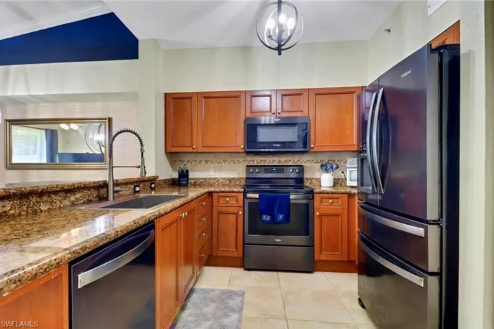 Kitchen with black appliances, brown cabinets, dark stone countertops, and a chandelier