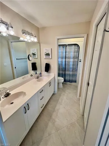 Bathroom featuring a sink, toilet, a shower with shower curtain, and double vanity