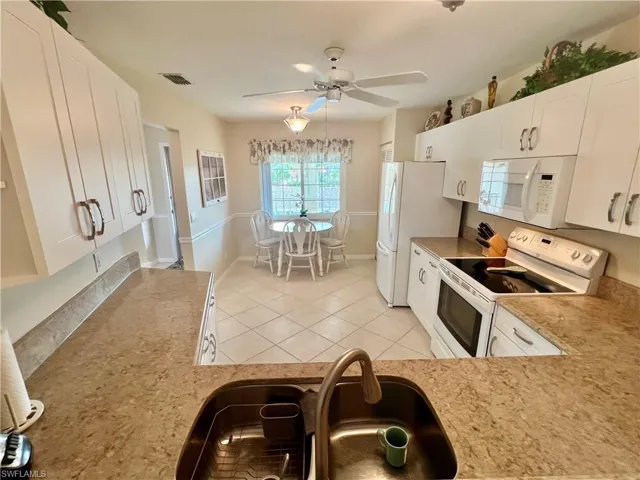 Kitchen with visible vents, light countertops, white appliances, white cabinetry, and a sink
