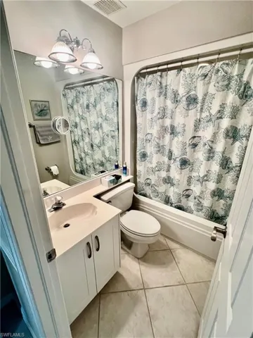 Bathroom featuring tile patterned flooring, visible vents, toilet, shower / bath combo with shower curtain, and vanity