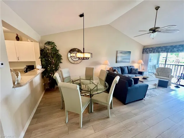 Dining room with light wood finished floors, ceiling fan with notable chandelier, baseboards, and lofted ceiling