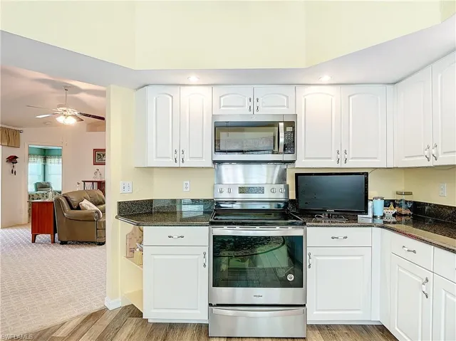 Kitchen featuring stainless steel appliances, dark stone countertops, white cabinetry, ceiling fan