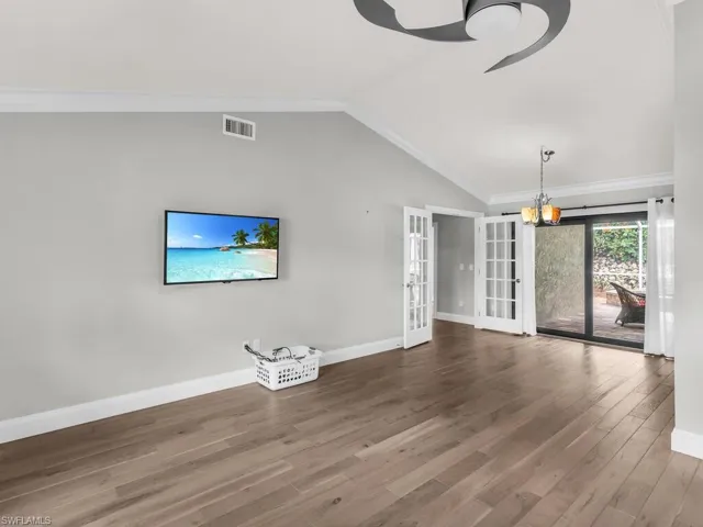 Unfurnished living room featuring hardwood / wood-style flooring, ornamental molding, an inviting chandelier, lofted ceiling, and french doors