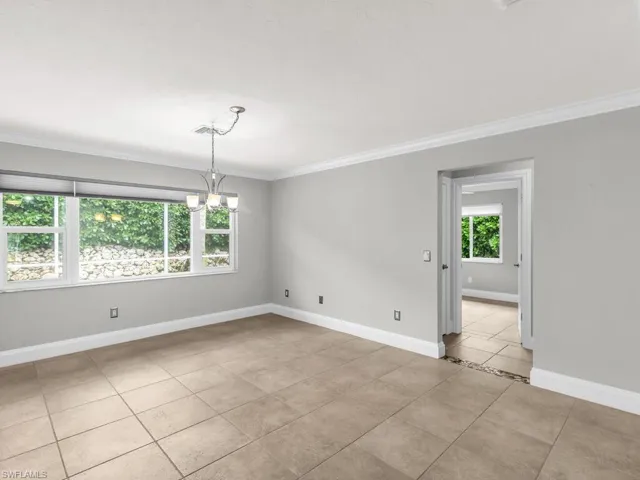 Tiled spare room featuring a wealth of natural light, a notable chandelier, and ornamental molding