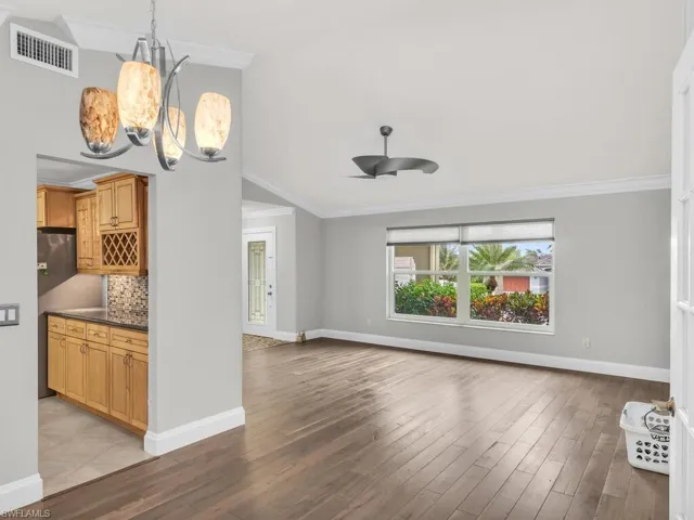 Unfurnished living room with ceiling fan with notable chandelier, light hardwood / wood-style flooring, and ornamental molding