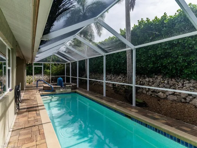 View of swimming pool with a hot tub, glass enclosure, and a patio area