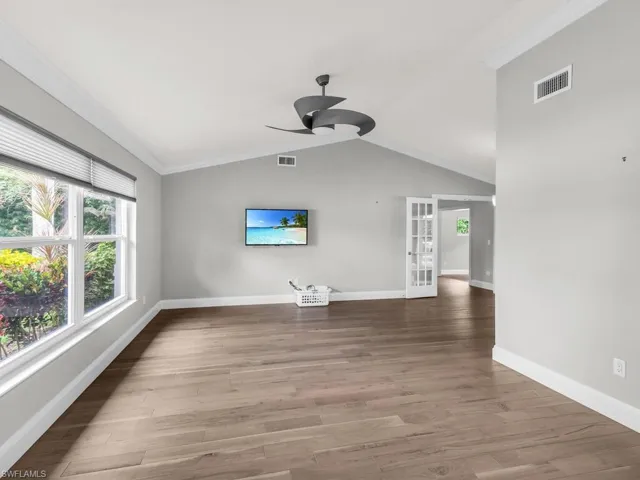 Unfurnished living room with ceiling fan, hardwood / wood-style floors, vaulted ceiling, crown molding, and french doors