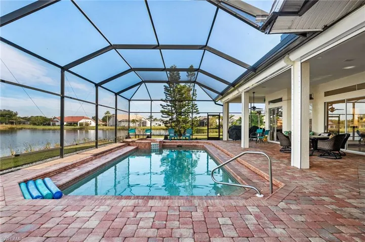 View of swimming pool featuring a patio, a water view, a hot tub, and a lanai