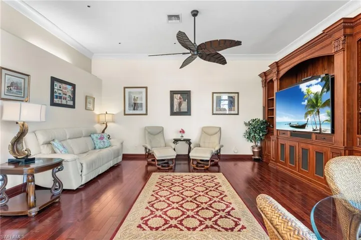 Living room with dark wood-type flooring, ceiling fan, and ornamental molding