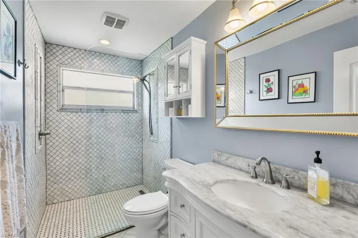 Bathroom with tile patterned floors, vanity, toilet, and a tile shower