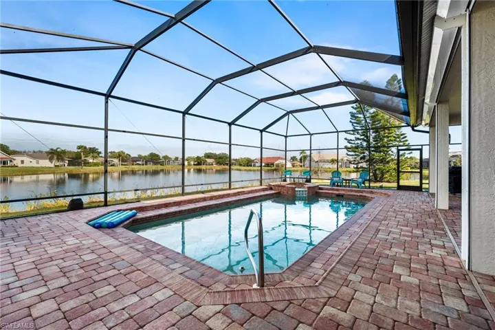 View of pool with glass enclosure, a patio area, and a water view