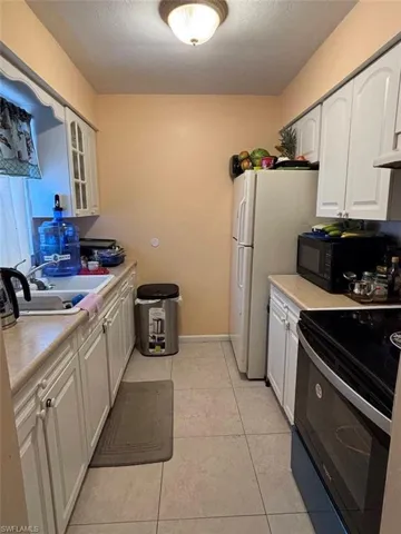 Kitchen featuring white cabinets, light tile patterned floors, white refrigerator, range with electric stovetop, and sink