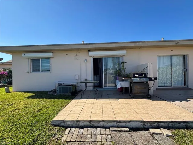 Rear view of house with a patio area, cooling unit, and a lawn