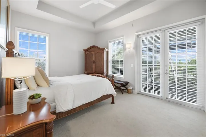 Carpeted bedroom featuring access to outside, multiple windows, a tray ceiling, and ceiling fan
