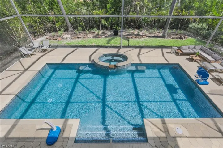 View of pool featuring glass enclosure, a pool with connected hot tub, and a patio area