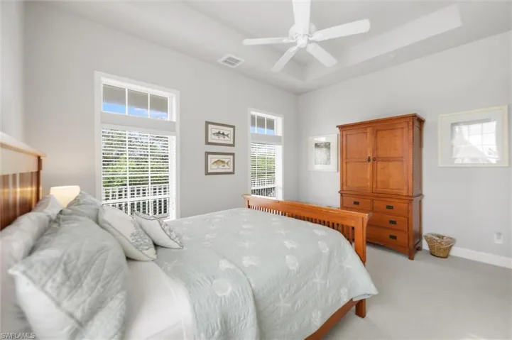 Bedroom with light carpet, a raised ceiling, and a ceiling fan