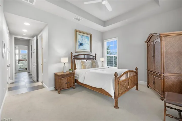 Bedroom featuring light carpet, multiple windows, a ceiling fan, and a raised ceiling
