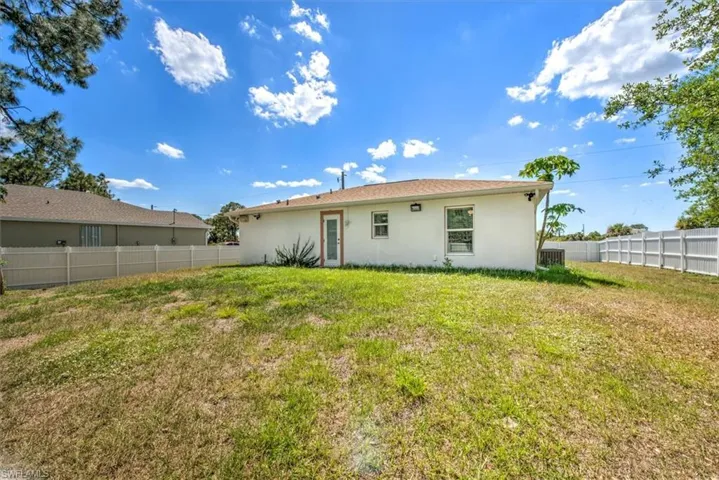 Rear view of house featuring stucco siding, fence, central AC, and a yard