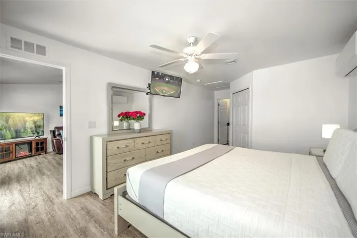 Bedroom featuring light wood-type flooring, a wall mounted AC, ceiling fan, and visible vents