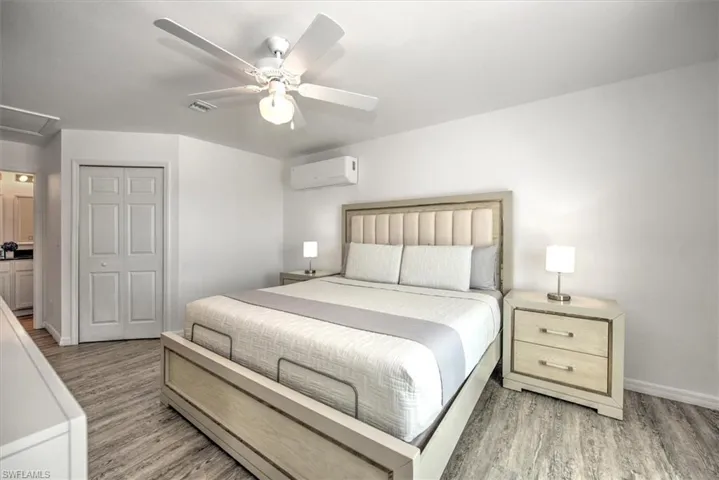 Bedroom with visible vents, light wood-style floors, an AC wall unit, and a ceiling fan