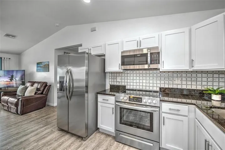 Kitchen with vaulted ceiling, light wood finished floors, open floor plan, stainless steel appliances, and white cabinets