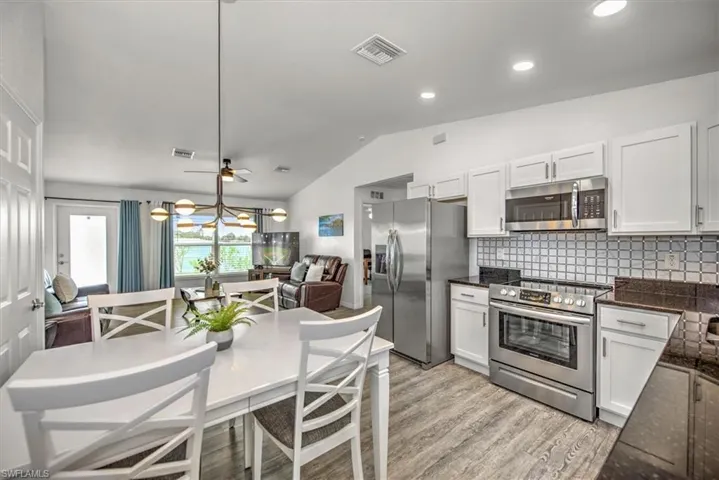 Kitchen featuring vaulted ceiling, decorative backsplash, light wood finished floors, white cabinets, and appliances with stainless steel finishes